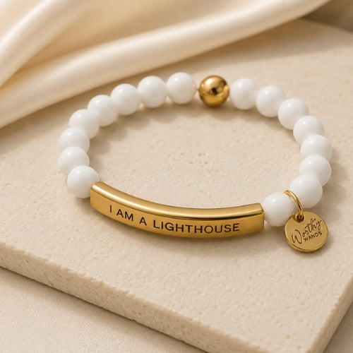 White beaded bracelet with gold bar and tag on a beige surface